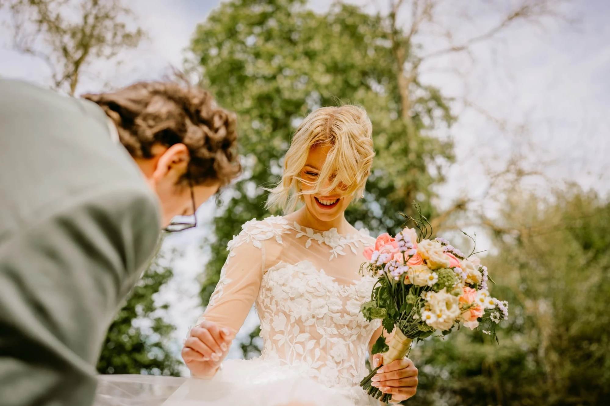 Mariée souriante tenant un bouquet de mariage, homme en costume à côté. photographe-lille