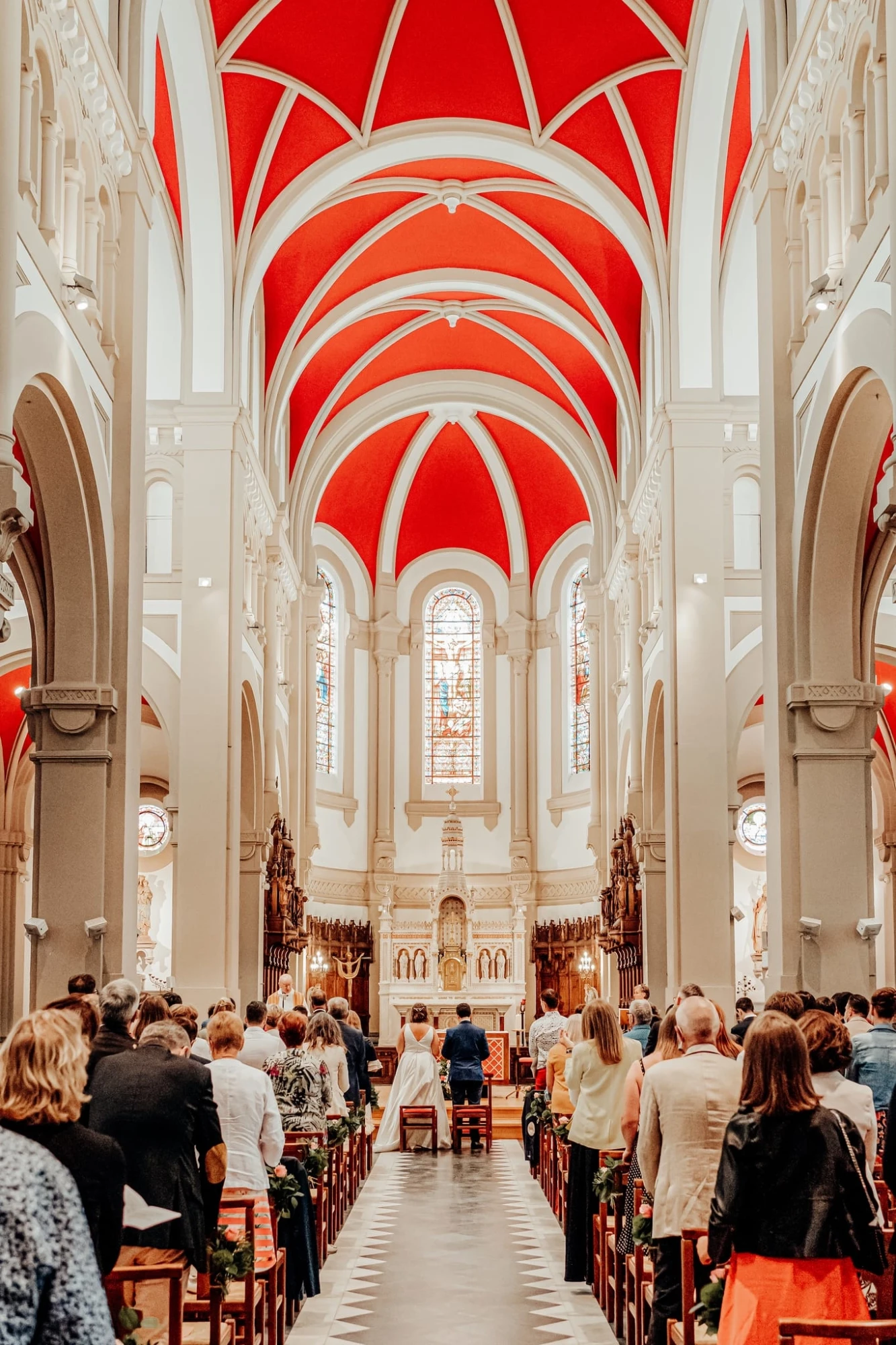 Mariage dans une église avec plafond rouge et invités présents. photographe-lille