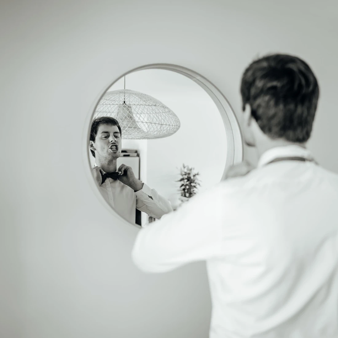 Homme ajustant son nœud papillon devant un miroir rond. Préparation pour un événement formel. photographe-lille