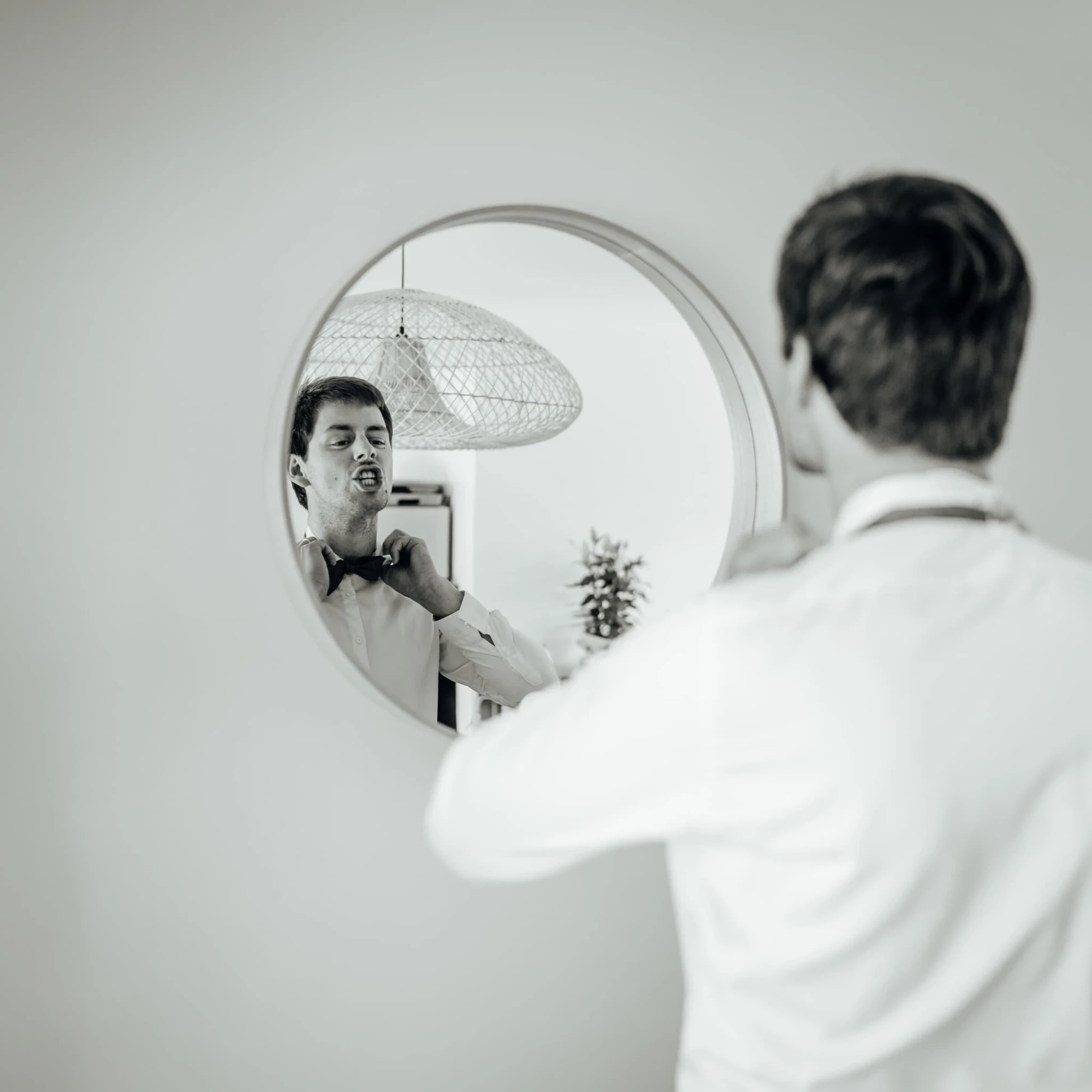 Homme ajustant son nœud papillon devant un miroir rond. Préparation pour un événement formel. photographe-lille