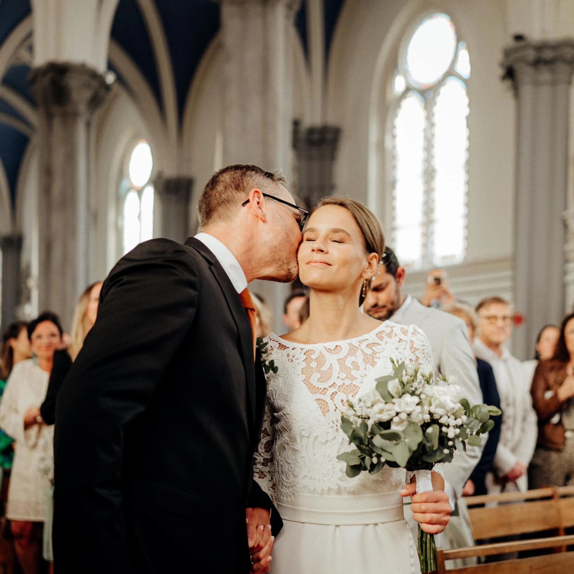 Marié embrassant la mariée dans une église, bouquet à la main. photographe-lille