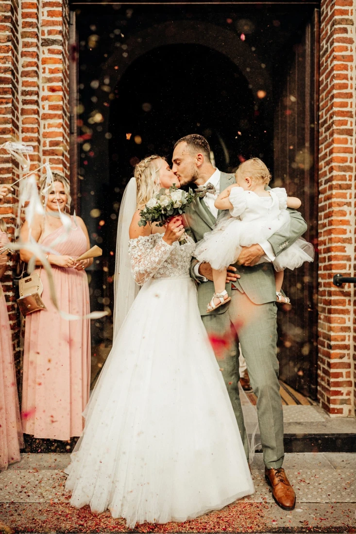 Mariés s'embrassant sous une pluie de confettis, bébé dans les bras. photographe-lille