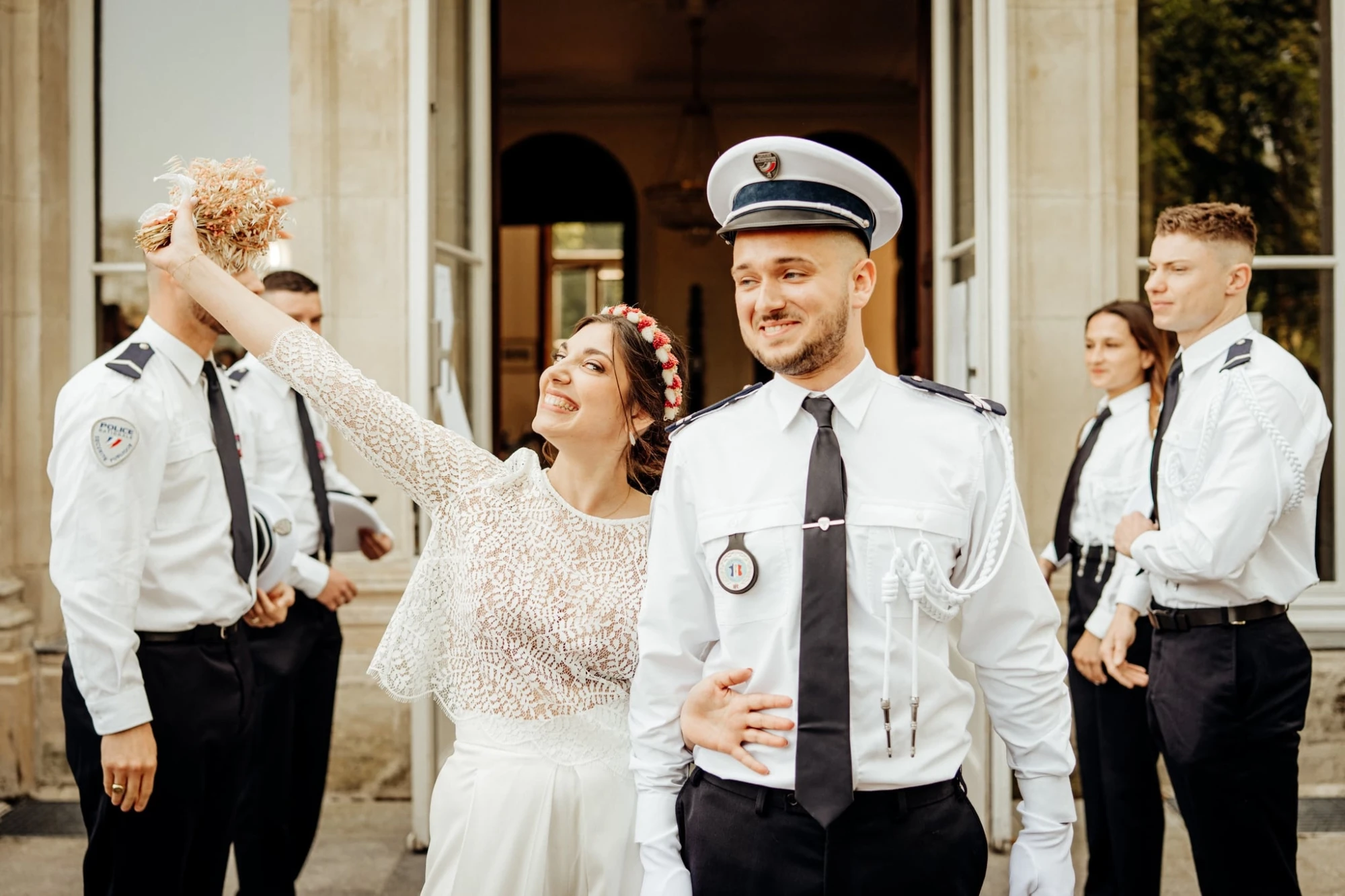 Les mariés en uniforme, souriants, avec le cortège nuptial en arrière-plan. photographe-lille