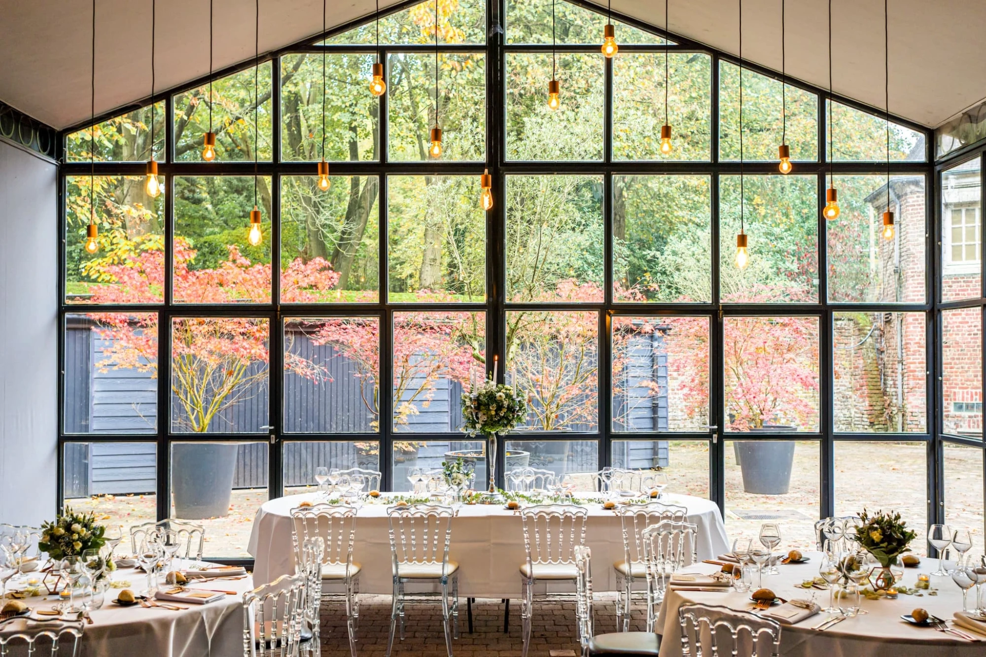 Salle de réception lumineuse avec tables dressées et grande baie vitrée donnant sur jardin automnal. photographe-lille