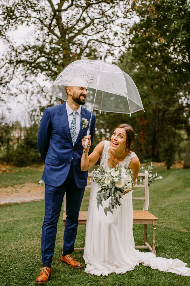 Mariés souriants sous un parapluie transparent, jour de pluie. photographe-lille