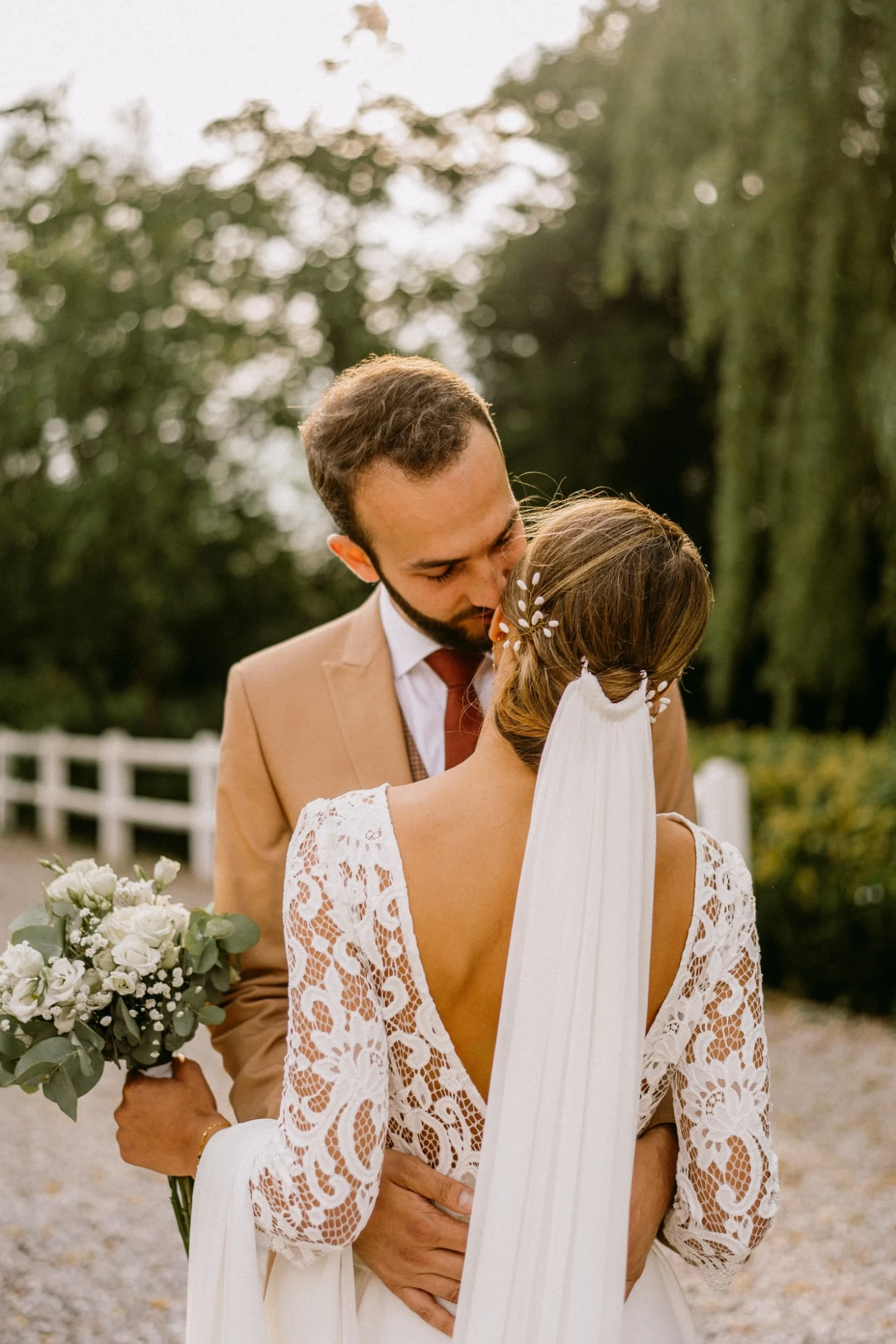 Mariés s'embrassant tendrement, robe en dentelle et bouquet blanc. photographe-lille
