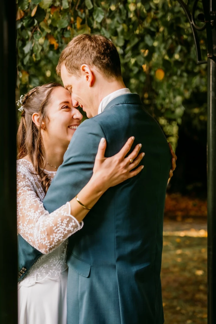 Un couple souriant s'embrasse à l'extérieur, sous une arche feuillue. photographe-lille