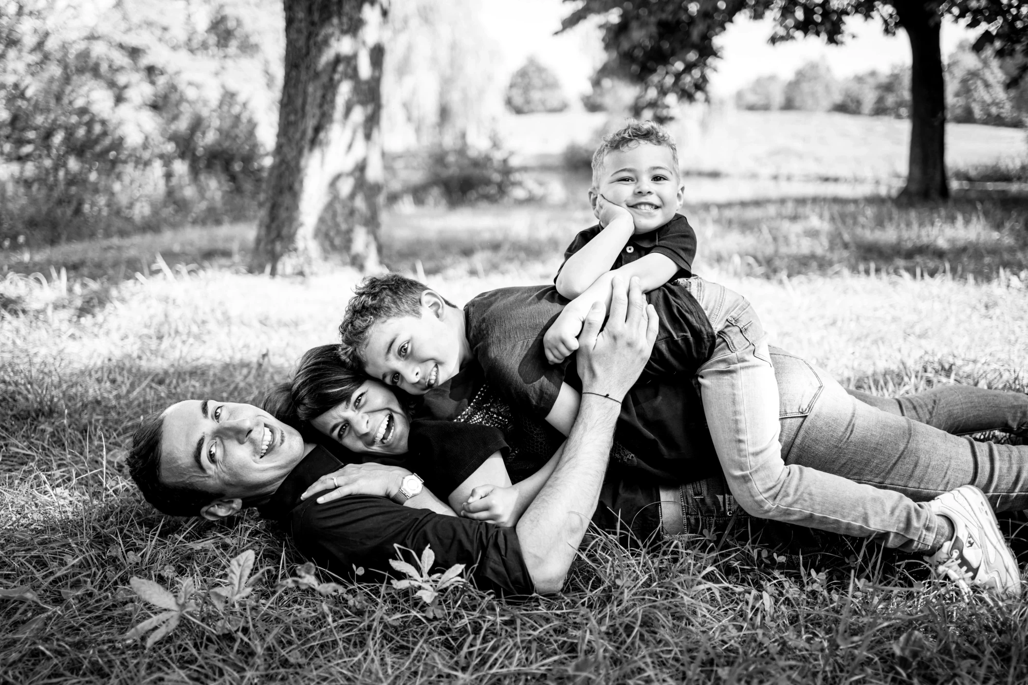 Famille souriante allongée dans l'herbe, profitant d'un moment joyeux ensemble. photographe-lille