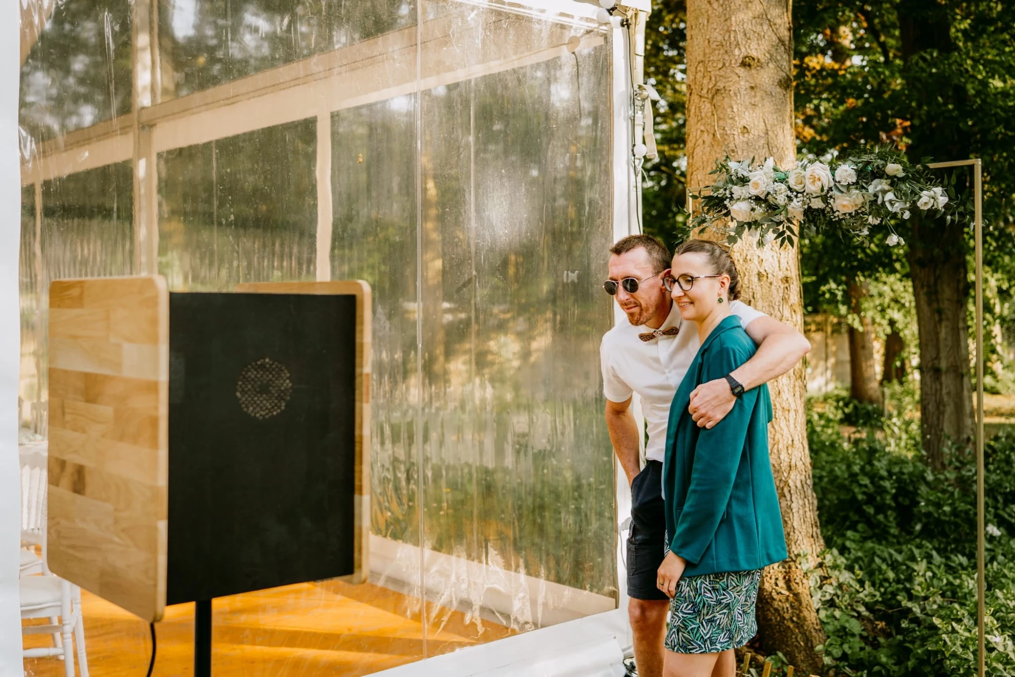 Couple souriant prenant des photos dans une cabine photo lors d'un mariage en plein air. photographe-lille