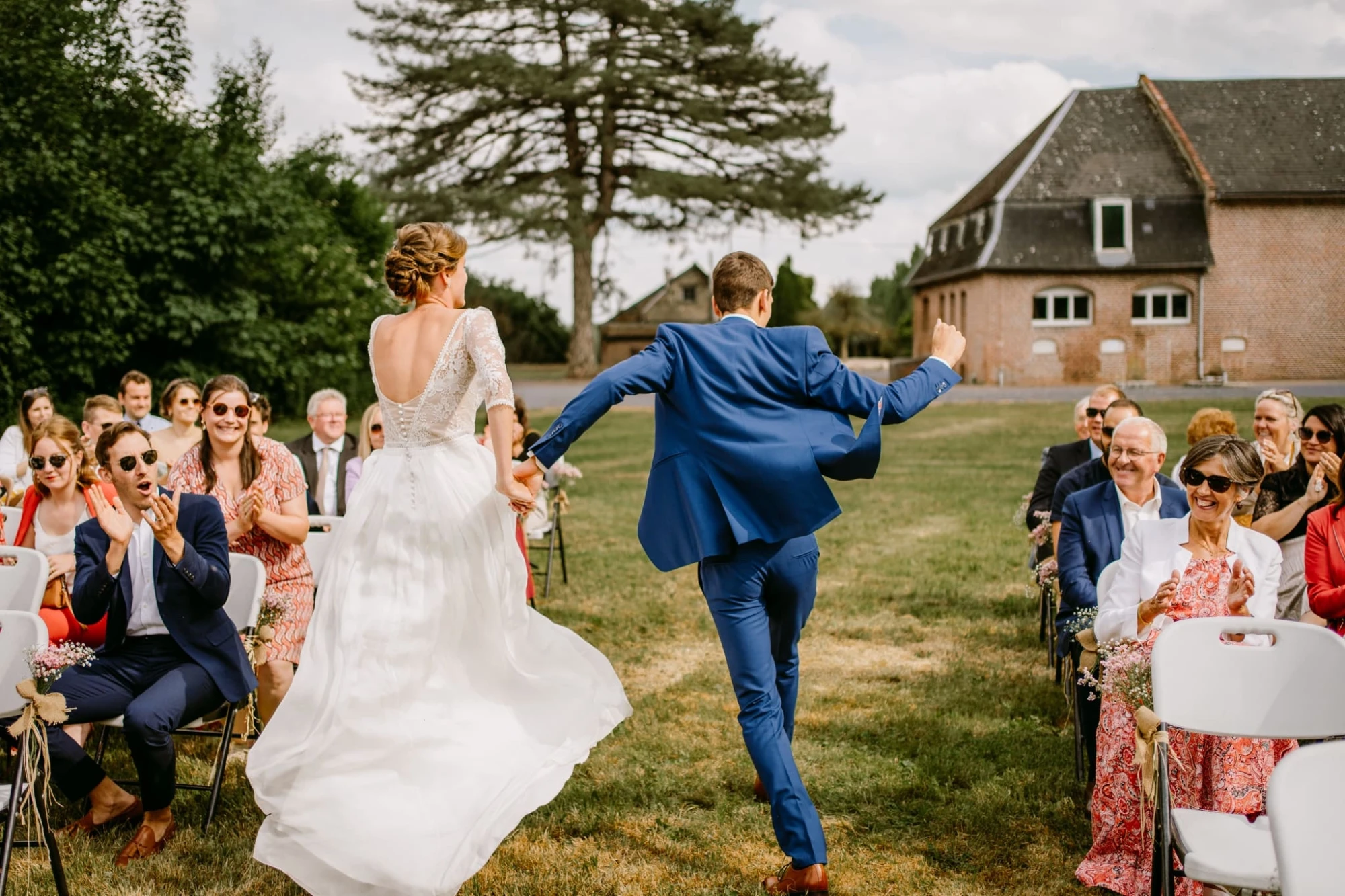 Mariés courant dans l'allée, applaudis par les invités lors d'un mariage en plein air. photographe-lille