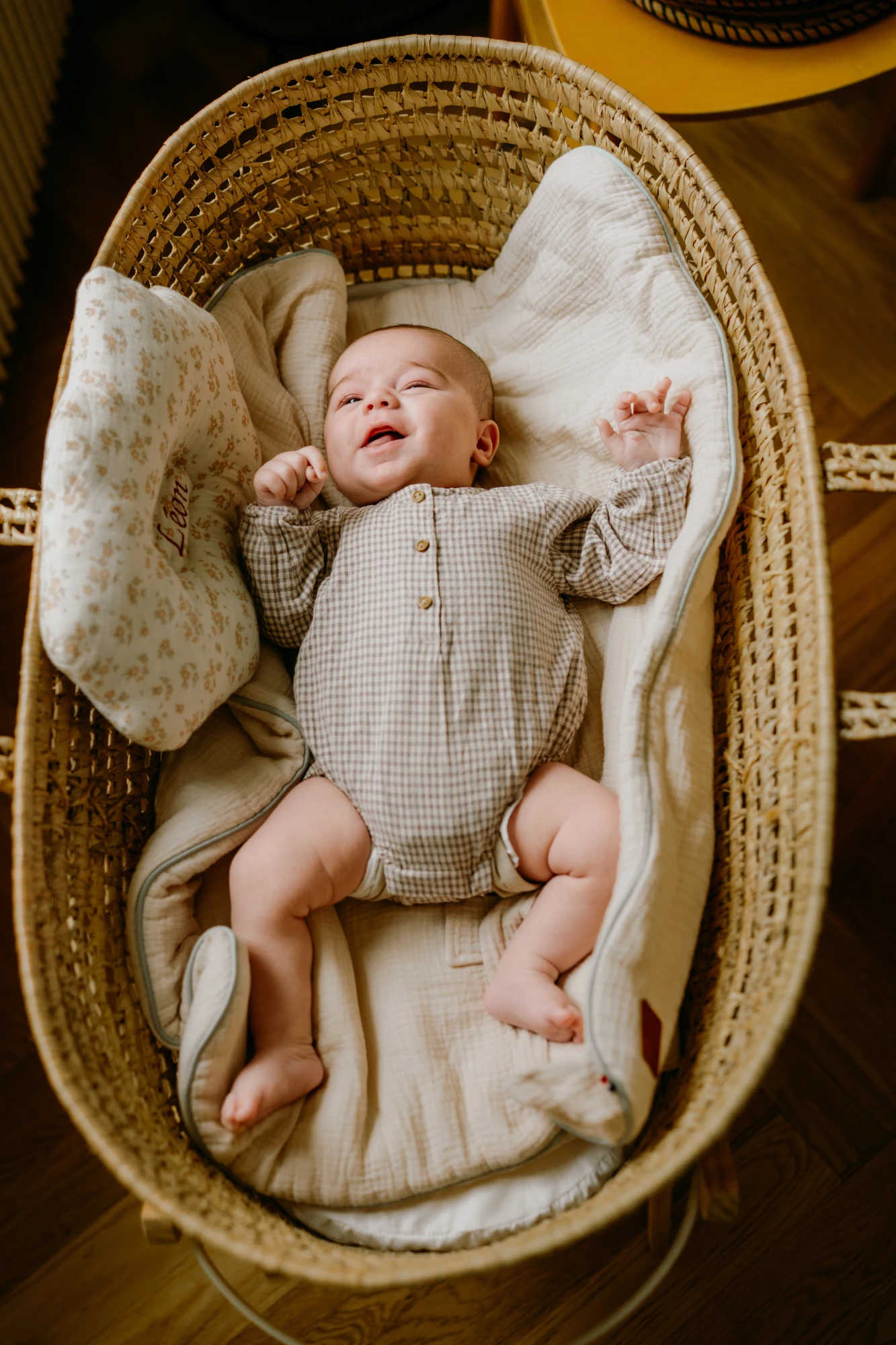Bébé souriant allongé dans un couffin en osier avec oreiller. photographe-lille
