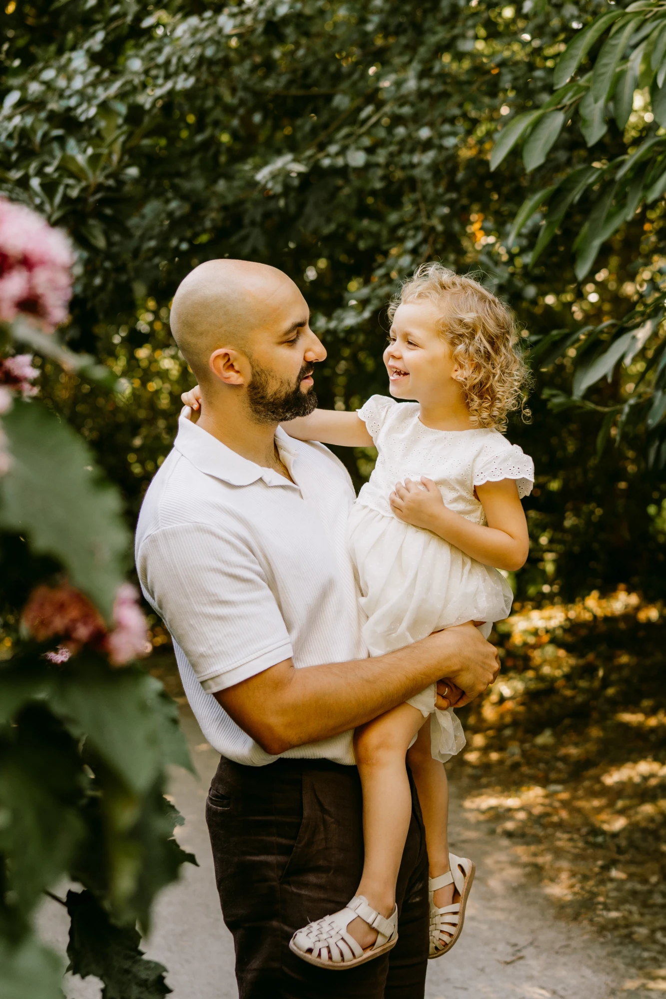 Père tenant sa fille dans un jardin verdoyant. Sourires complices. photographe-lille