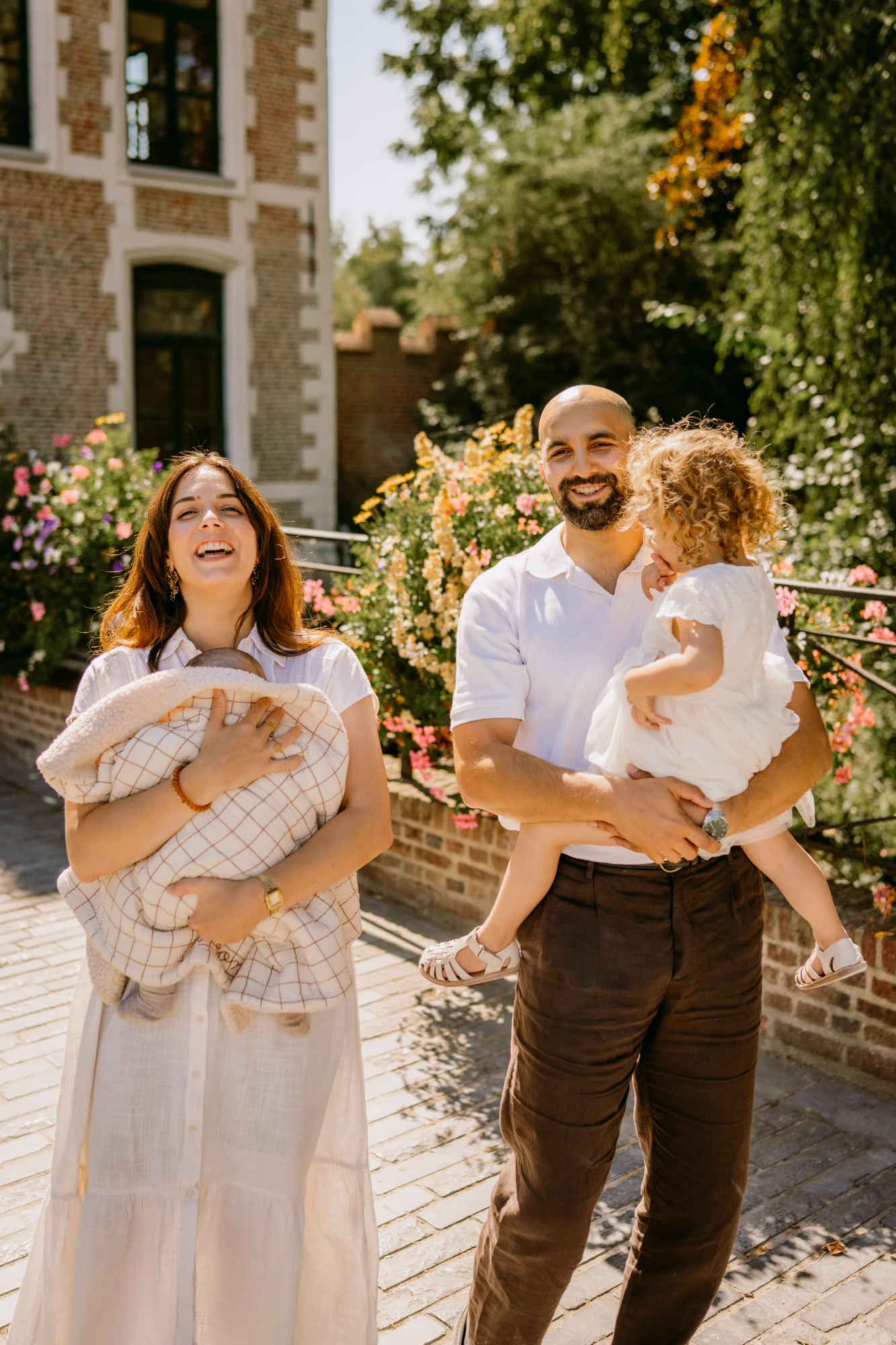 Famille heureuse avec bébé et petite fille devant un bâtiment en briques fleuri. photographe-lille